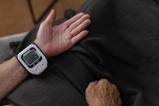 Man covered by gray and black blanket sitting in wellness centre with hand palm facing up measured for blood pressure with a result of high blood pressure